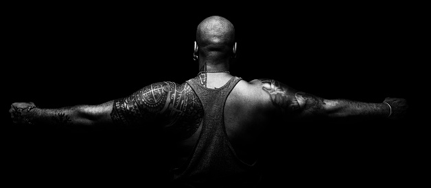 Back and arms of black man tattooed on black background in balnco and black