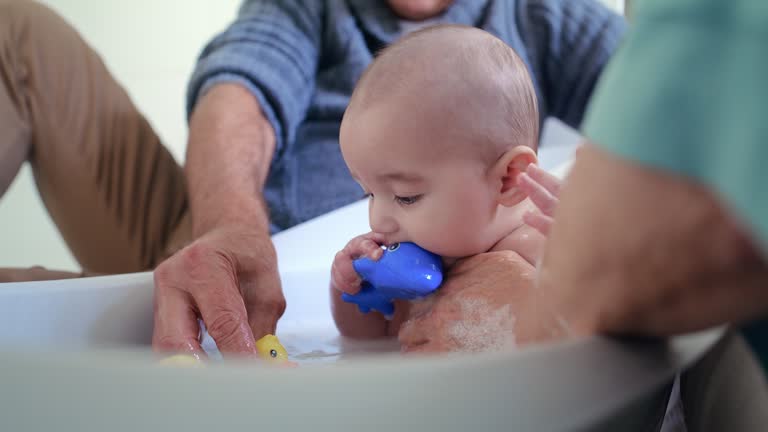 Bath, washing and parents with soap for baby for cleaning, hygiene and wellness in tub at home. Family, childcare and mom and dad with newborn, child and kid with toys, water and health in bathroom