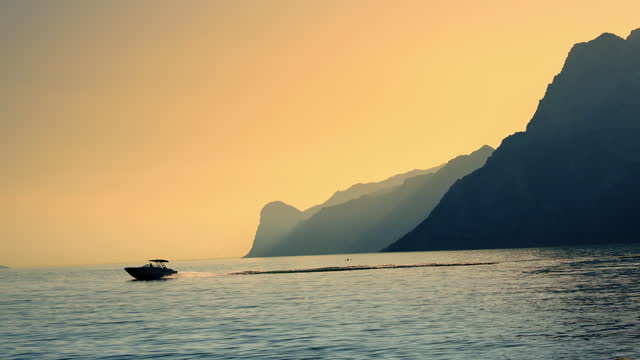 SLO MO Motorboat on Lake Garda along Silhouette Mountains and Orange Sky at Sunset