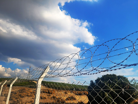 barbed wire steel wall against immigations. Wall with barbed wire on the border of 2 countries. Private or closed military zone against the background blue sky.