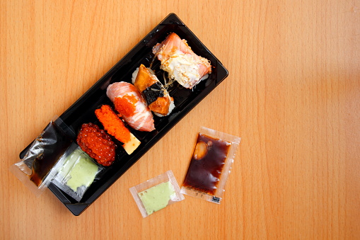 Sushi on rectangle shape black plastic box and wasabi, soy sauce on bright brown wood.