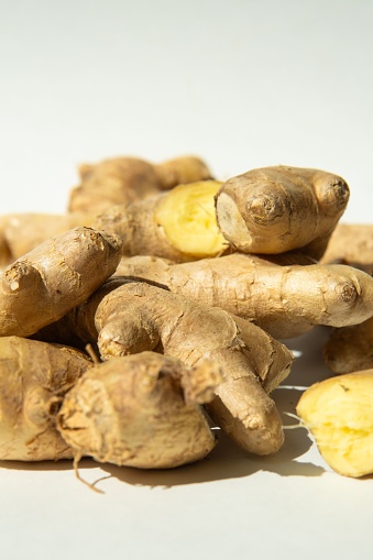 A stack of freshly cut ginger root pieces on a wooden table with visible stems