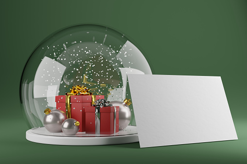 Front view of a glass snow globe holding a blank greeting card with copy space against a green background