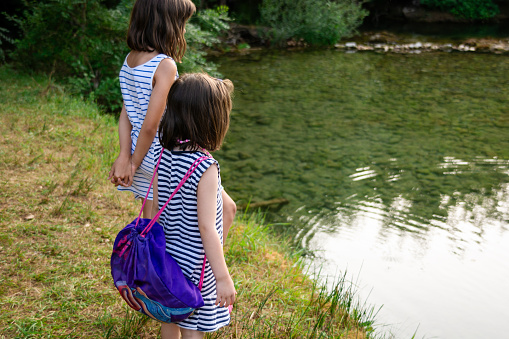 Two girls stand on the riverbank and look at the river during summer day. Copy space