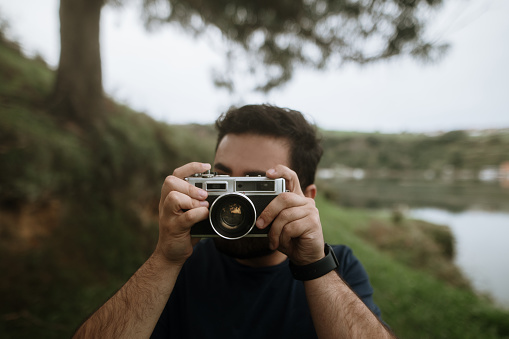 A young man taking a photo using a vintage film camera in a natural area