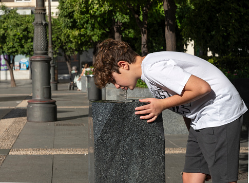 Teenage boy drinking water from a fountain in the street