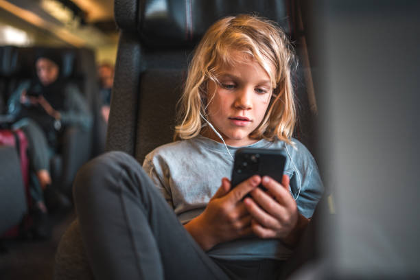 A boy on a train journey, killing time watching content with a smartphone and earphones.