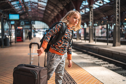 In Copenhagen, a young traveler with long blond hair stands at the station, luggage by his side, awaiting the train.