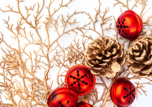 Festive green Christmas wreath decorated with red bows, various gold and red baubles, and two large brass bells, hanging on a textured wall