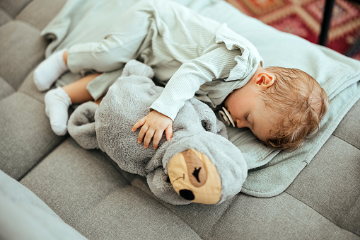 Cute healthy little Asian 18 months / 1 year old toddler baby boy child sleeping / taking a nap under blanket in bed while hugging teddy bear, Daytime sleep, kid deep sleeping, sweet dream concept