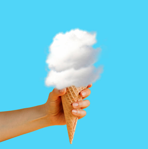 istock Female hand holding waffle cone with clouds on blue background. Creative minimal art poster. 1740455518
