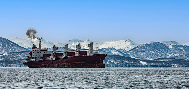 The container ship in the bay opposite the snow-capped mountains on the Kamchatka Peninsula