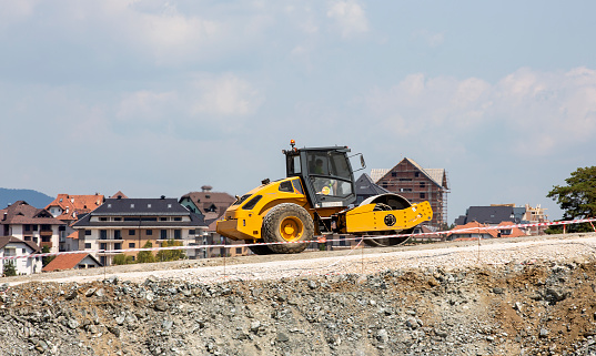 The heavy concrete paver machine on the road against the background of beautiful houses. Selective focus