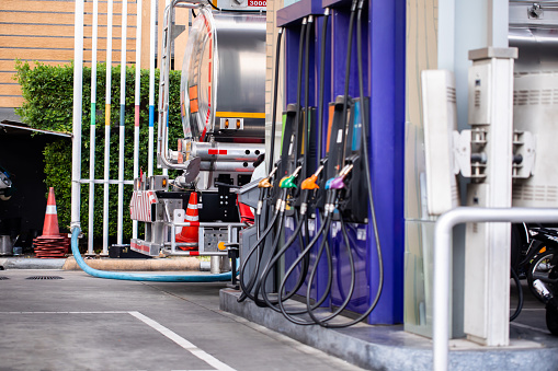 Selective focus to fuel tanker truck with blurry fuel dispenser is transferring fuel to storage tanks in a gas station.