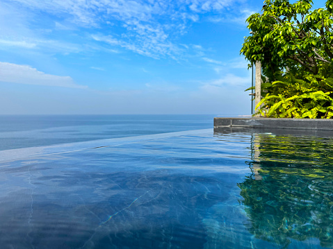 Stock photo showing a luxury infinity swimming pool on a sunny afternoon, designed so that the edge seems to merge with the sky. These types of pools are also known as infinity edge or zero edge pools.