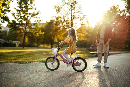 Father and daughter in the park, she is riding a bicycle