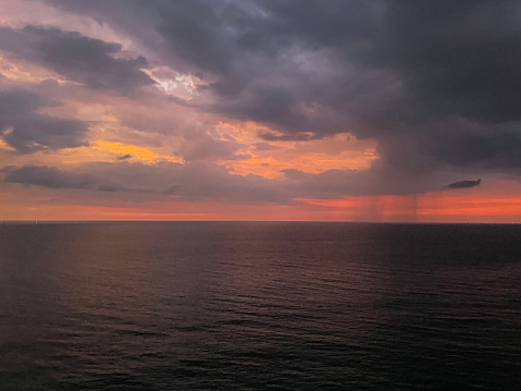 Stock photo showing a moody, dramatic orange and purple sky as sun sets below grey bank of cloud on the horizon over the sea.