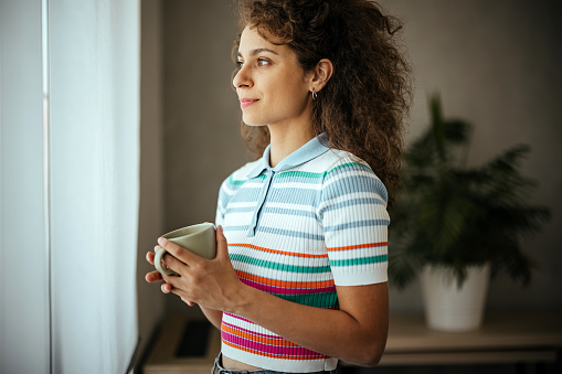 Portrait of young woman with coffee standing in the living room