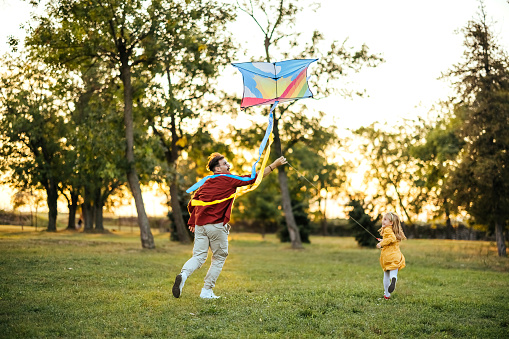 Father playing with daughter in natural park with kite - toy