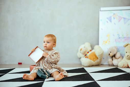 Portrait of a baby girl dressed in a dress sitting on the floor