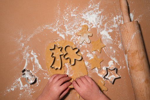 Family with kids preparing Christmas Cookies on table sprinkled with flour. Children hands making gingerbread with cookies cutters from dough. Flat lay, minimalist