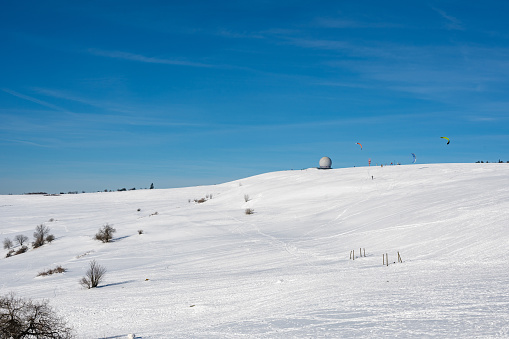 Snow kiting on the Wasserkuppe with radar dome in Germany on a beautiful winter day with blue sky and lots of snow
