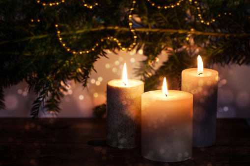 Three burning candles in front of dark fir branches with Christmas decoration and bokeh bubbles, seasonal holiday greeting card, copy space, selected focus, narrow depth of field