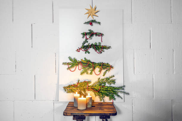 Homemade Christmas tree alternative, white cardboard plate with fir branches and decoration leaning against the wall on an old wooden stool with candles, copy space Homemade Christmas tree alternative, white cardboard plate with fir branches and decoration leaning against the wall on an old wooden stool with candles, copy space, selected focus alternative lifestyle stock pictures, royalty-free photos & images