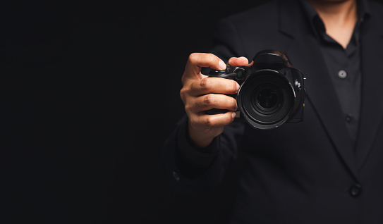 Photographer in a suit holding the digital camera while standing on a black background. Close-up photo
