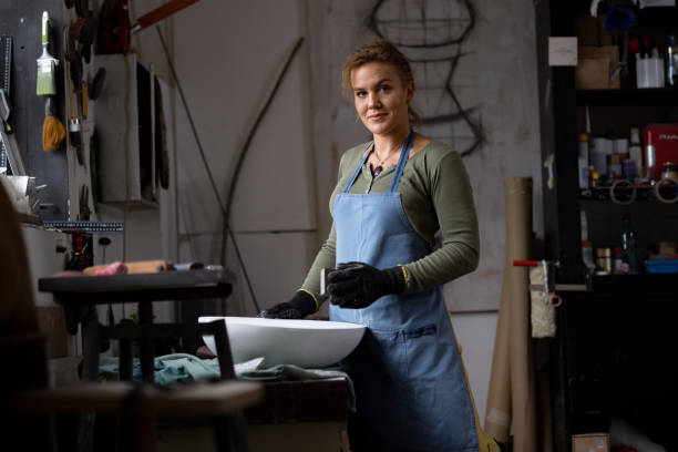 Smiling female potter polishing her sculpture in an art studio and looking at camera.