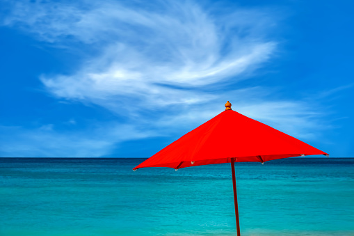 A red beach umbrella with blue sky and turquoise sea.