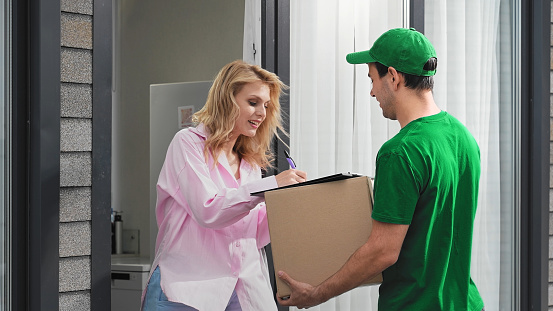Home fast delivery service. Man courier bring package. Girl open door take pack. Woman buy post parcel. Delivery guy give order. Postal box deliver. Happy postman put signature. Person receive carton.