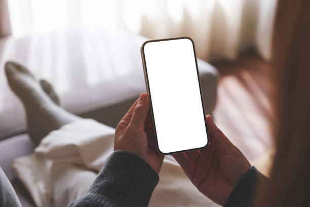 istock Mockup image of a woman holding mobile phone with blank desktop white screen while lying on a sofa at home 1740543999