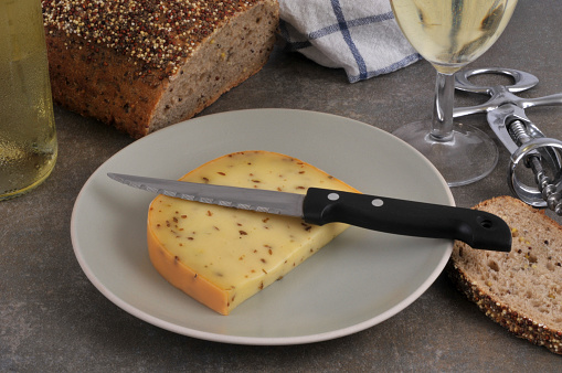 Piece of Gouda with cumin on a plate with a knife and a glass of wine and seeded bread