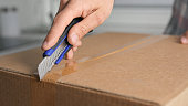 Person open cardboard box close up. Man unpack parcel. Hands hold clerical knife