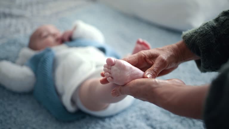 Baby feet, hands and lotion with massage and person at family home with love, care and support together. Bed, foot and happy young kid in a house with skin cream for newborn on a blanket and relax