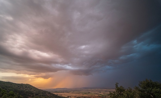 Incredible sunset amidst storm clouds and rain curtains with orange and black sky. Views of a huge dry field at sunset discharging a thunderstorm.