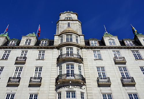 Oslo, Norway: Grand Hotel façade with clock tower, architect Johan Nordan - the hotel hosts the annual Nobel Peace Prize banquet, and the prize winners stay in the Nobel suite at the hotel. The hotel was founded by confectioner Julius Fritzner and opened in 1874. In the 1880s and 1890s, the Grand Café on the corner was an important meeting place for artists and intellectuals. Henrik Ibsen was known for his daily visits in the late 1890s, while he lived in Arbins gate . At the main table, the hotel gave him his own chair with a silver nameplate and a set of glasses with his name engraved on it.