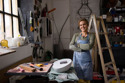 Happy female sculptor standing with her arms crossed in an art studio and looking at camera.