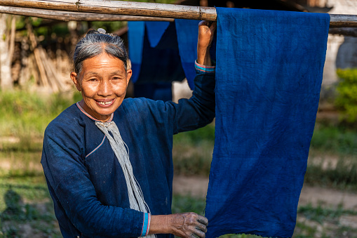 Laotian woman, wearing traditional Lantan tribe clothes, checking freshly dyed hand-woven cotton fabric in a Lantan village in Northern Laos