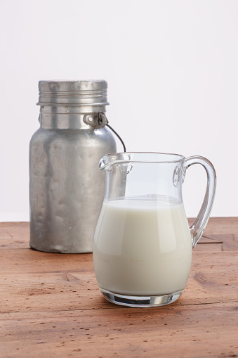 milk in glass jug with aluminum can on wooden table with white background