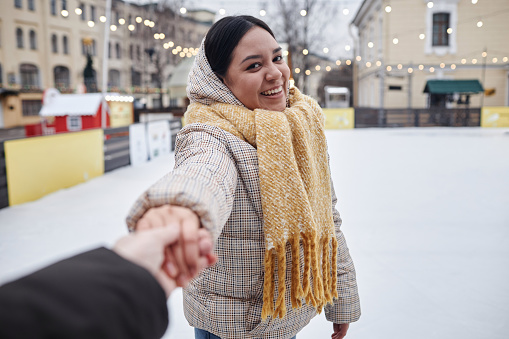 POV of young woman skating outdoors in winter holding hands with boyfriend on ice skating rink, copy space