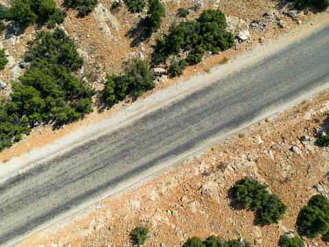 Bird's eye view of the road. There are maquis flowers on the sides of the asphalt road. Mediterranean region. Aerial shot with drone.