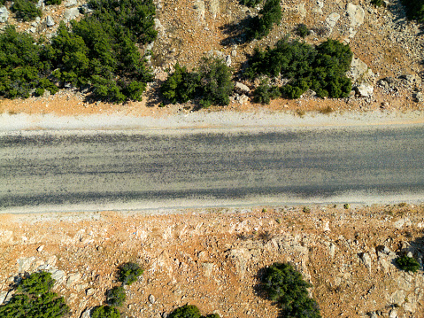 Bird's eye view of the road. There are maquis flowers on the sides of the asphalt road. Mediterranean region. Aerial shot with drone.