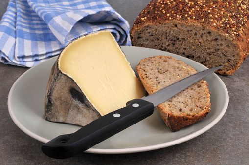 Piece of mountain tomme on a plate with a couetau and a slice of seeded bread