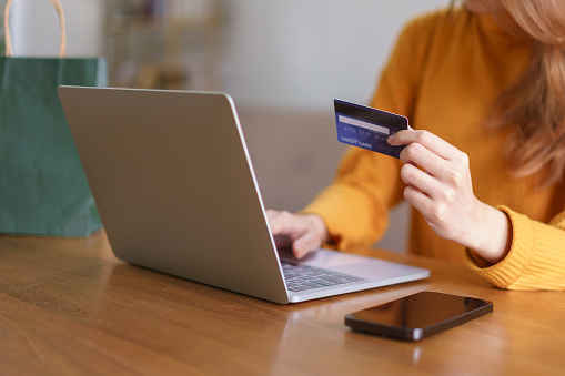 Cropped view of a cashier, a young woman, working in a coffee shop, taking a credit card or gift card from a customer. The main focus is on the hands and the card.