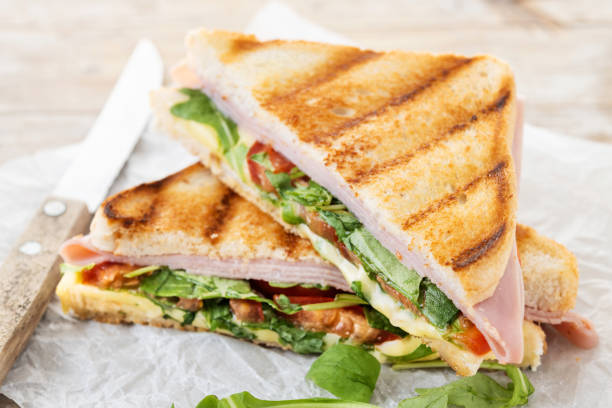 istock Panini sandwich with ham, cheese, tomato and arugula on wooden table 1740626379