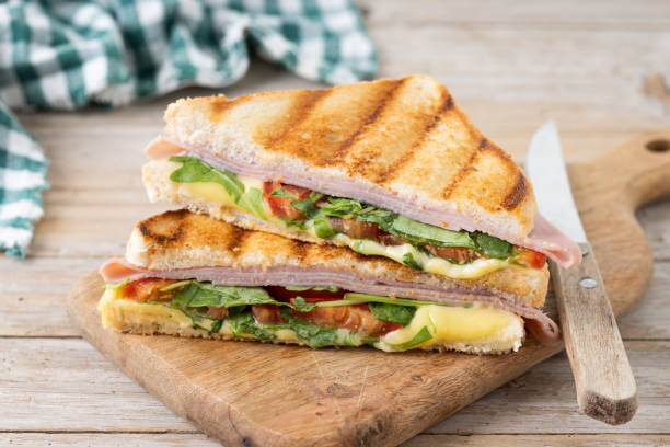 istock Panini sandwich with ham, cheese, tomato and arugula on wooden table 1740626942