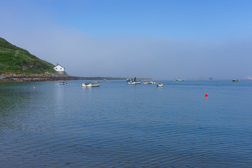 Fishermen prepare to go fishing while a bank of fog sits under a blue summer sky in Porthdinllaen harbour.