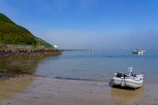 fishing and pleasure boats moored in Porthdinllaen harbour under a blue summer sky. Beyond the harbour a bank of fog lurks.